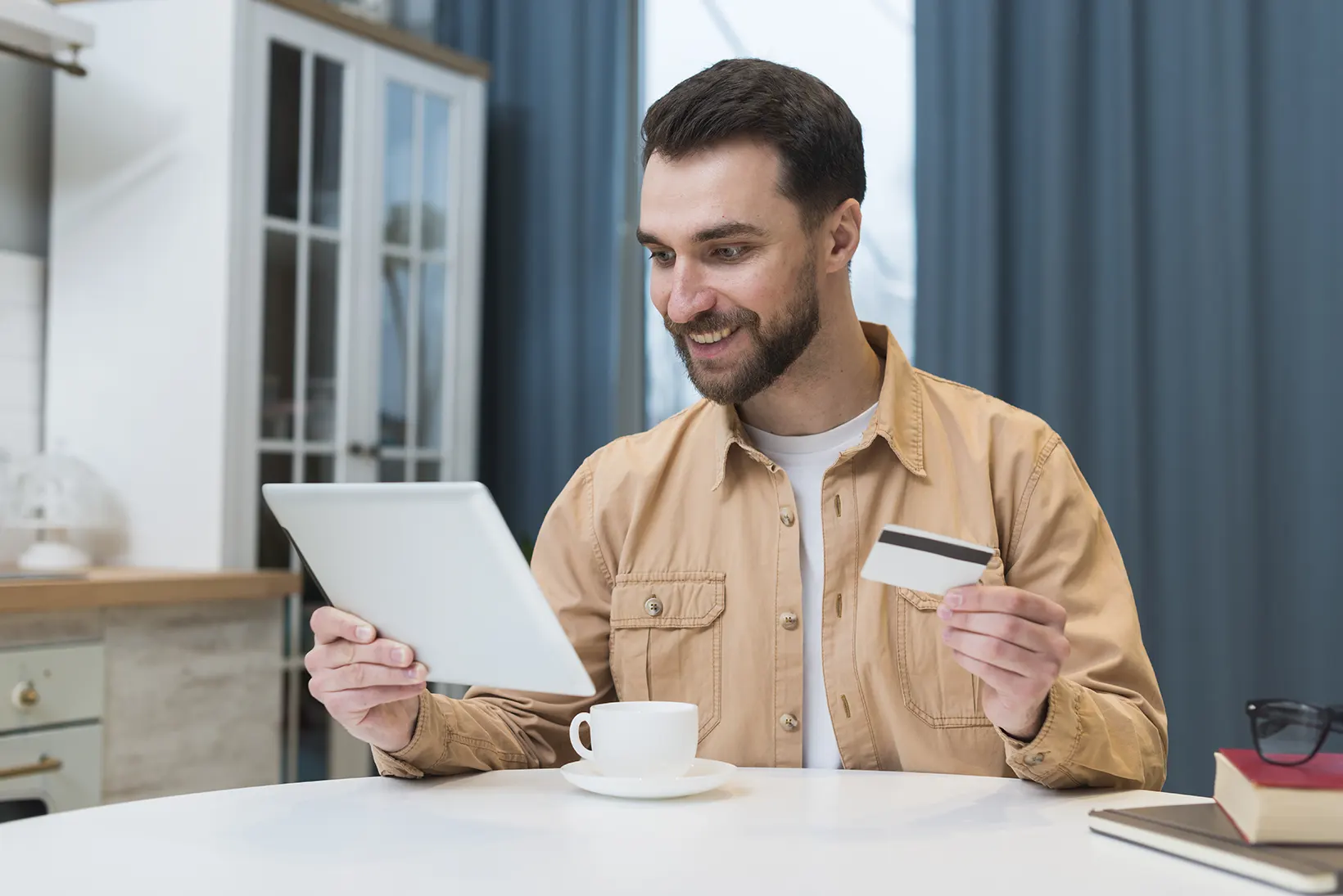 Se muestra un hombre contento mientras compra online desde una tablet con una tarjeta de credito en su mano